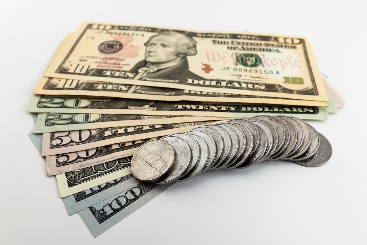 US dollar bills and coins spread out on a white surface
