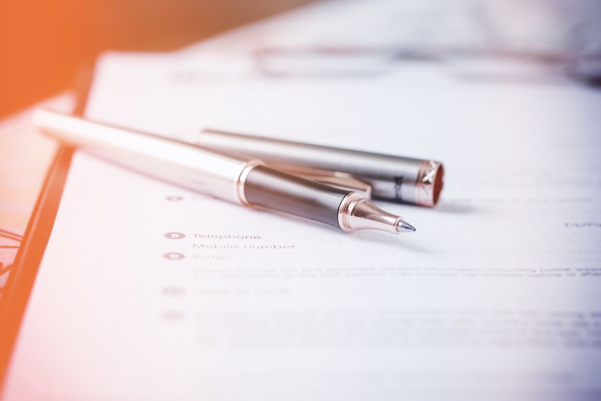 A paper form with two pens resting on top, soft light