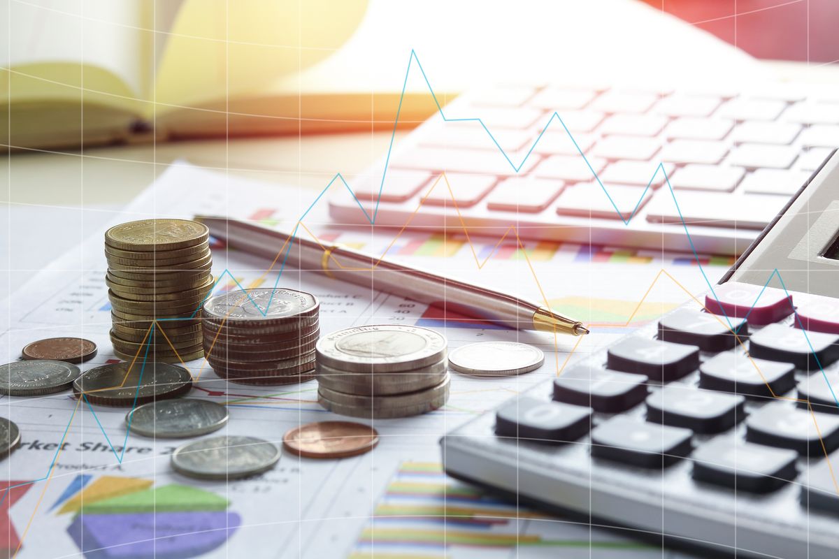 Piles of coins beside a calculator, pen and printed charts