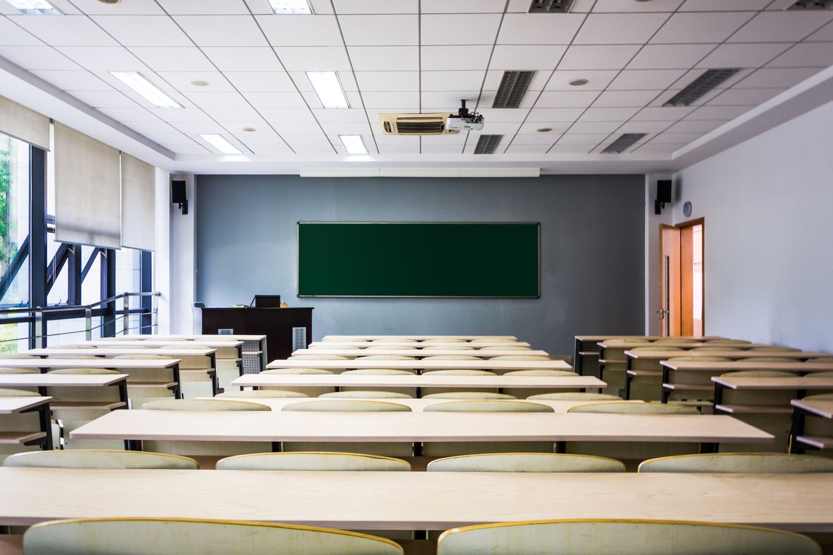 An empty classroom with rows of desks and a blank green chalkboard