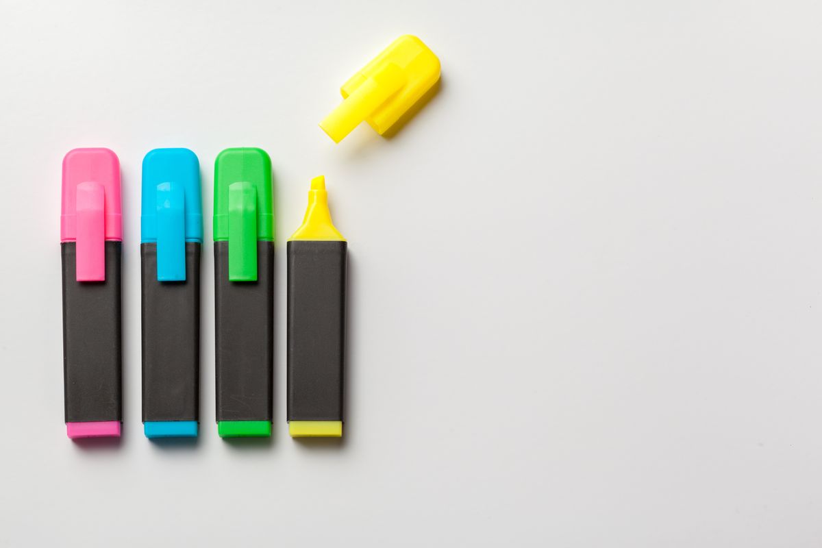 A row of pink, blue, green and yellow highlighter pens on a white surface