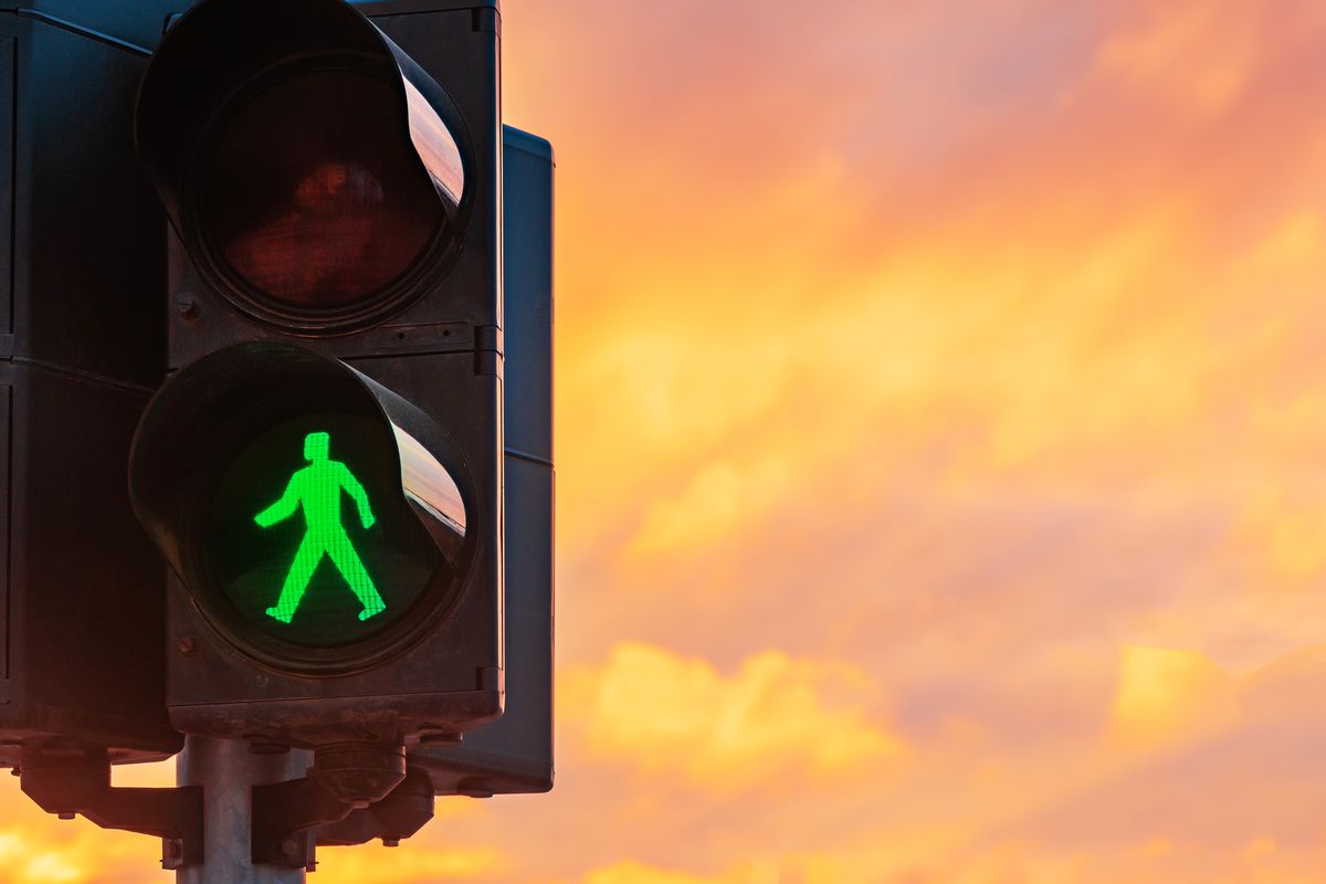 A green walking figure pedestrian signal against an orange evening sky
