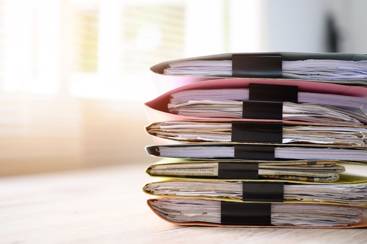 A tall stack of bound paper files with black clips resting on a bright office desk
