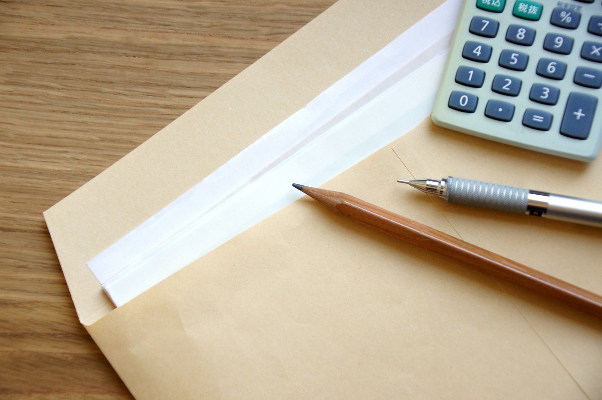 A manila envelope on a wooden desk with a pen, pencil and calculator