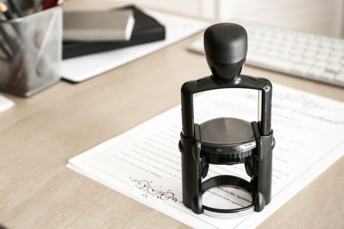 A black seal stamp press standing on a signed document on a desk
