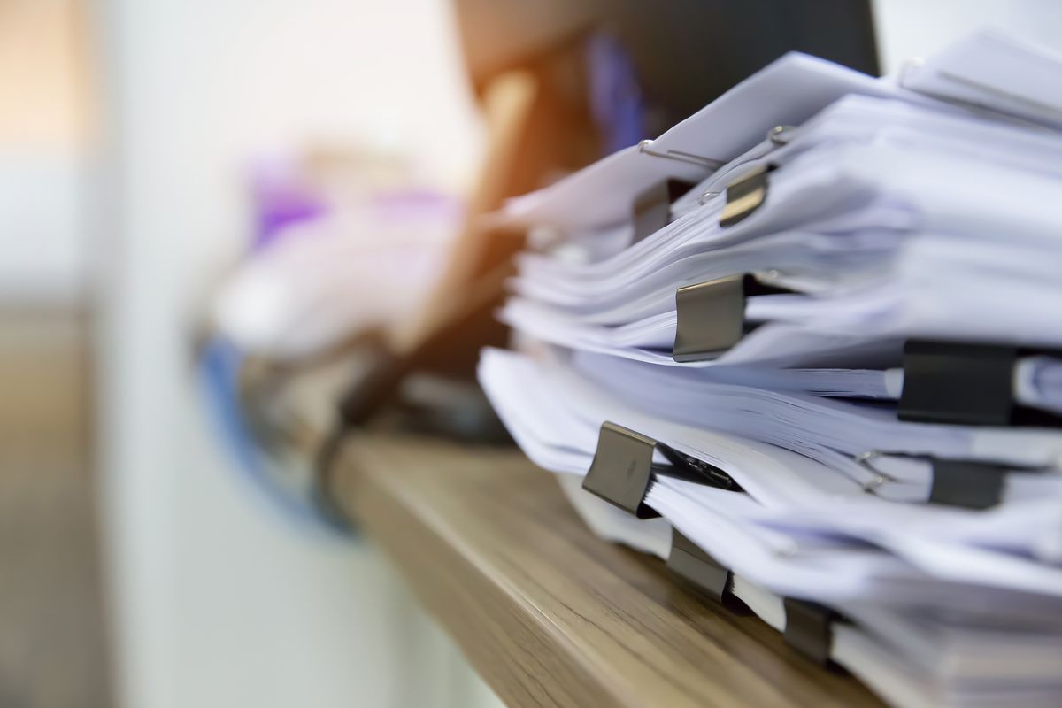 A tall stack of papers held with black clips on a desk