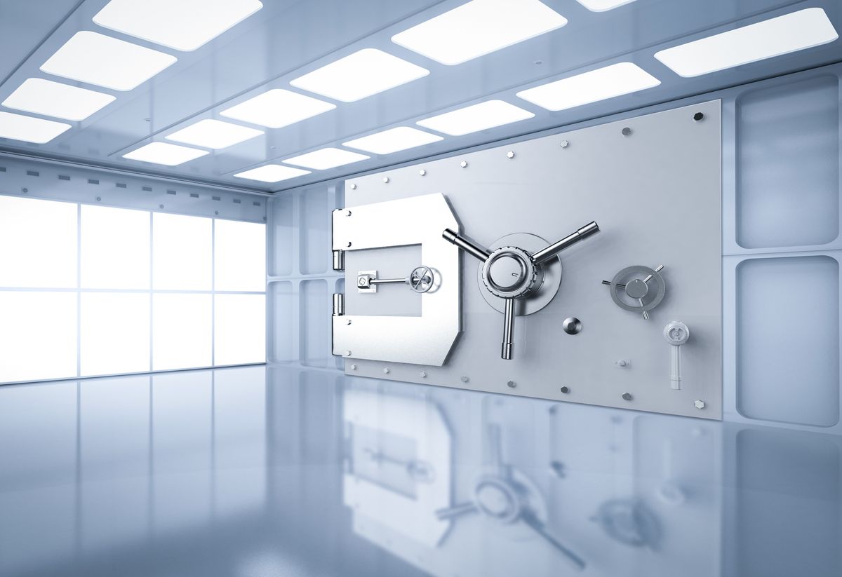 A large steel bank vault door with a wheel handle in a bright empty room.