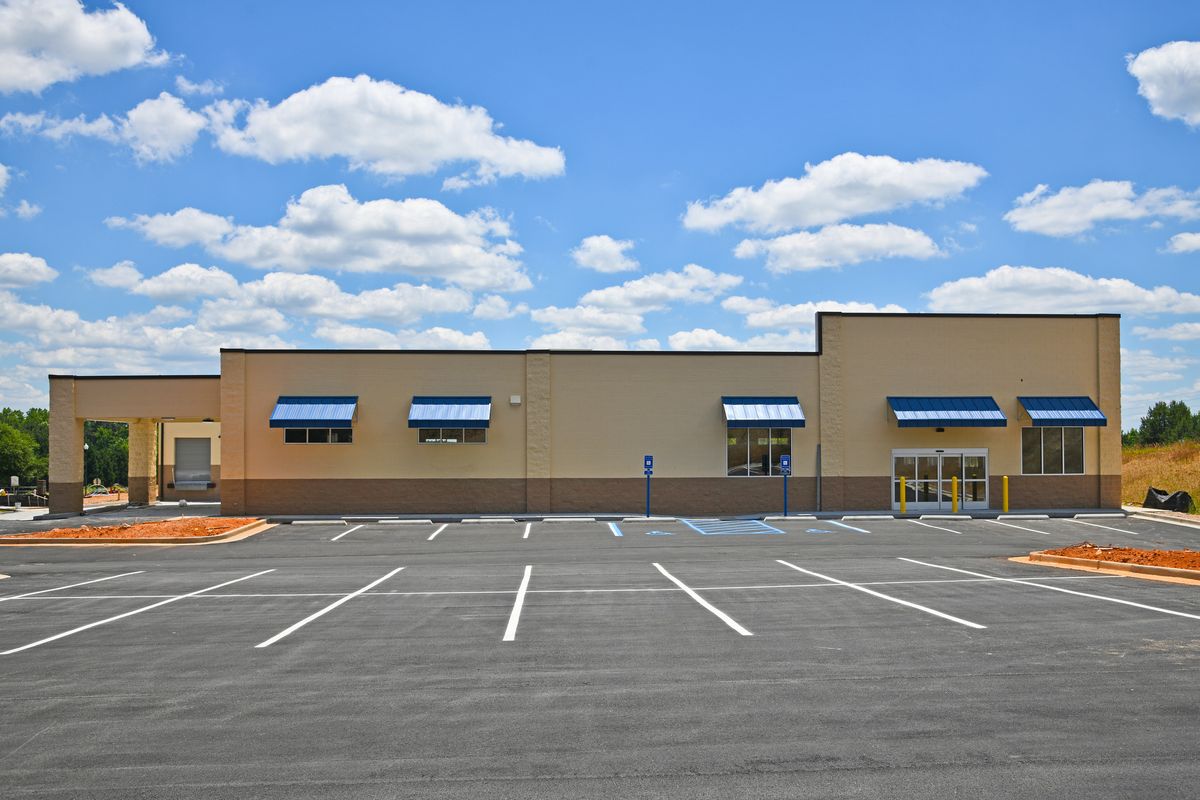 A new single story commercial building with storefront awnings and an empty parking lot under a blue sky.