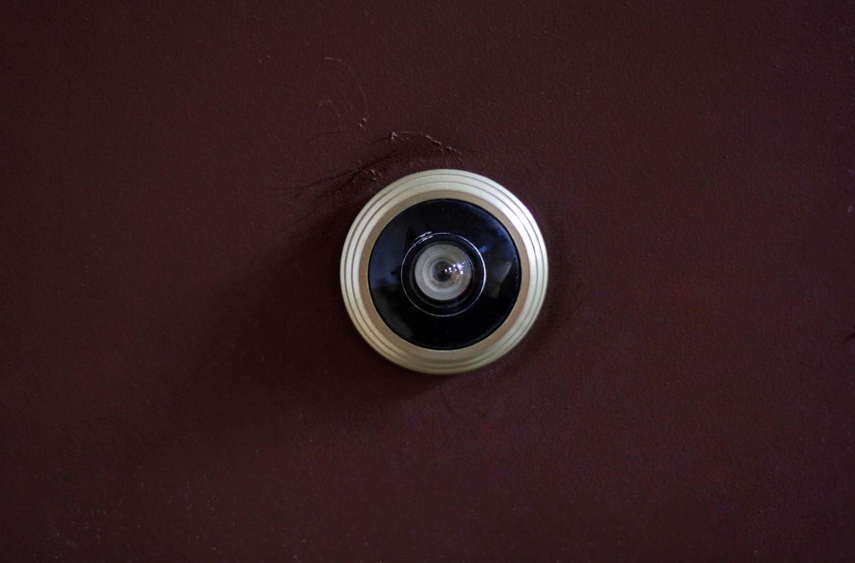 A close up of a metal door peephole set into a dark brown wooden door