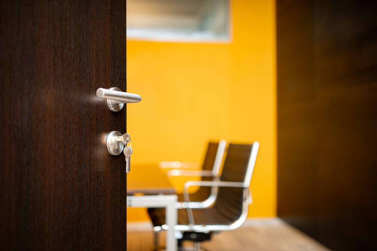 An open wooden office door with keys in the lock revealing an office chair inside.