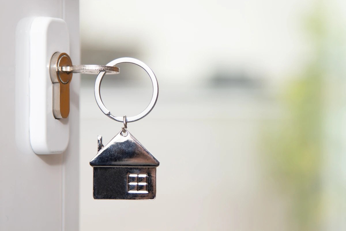 A house shaped keychain hanging from a key in a door lock