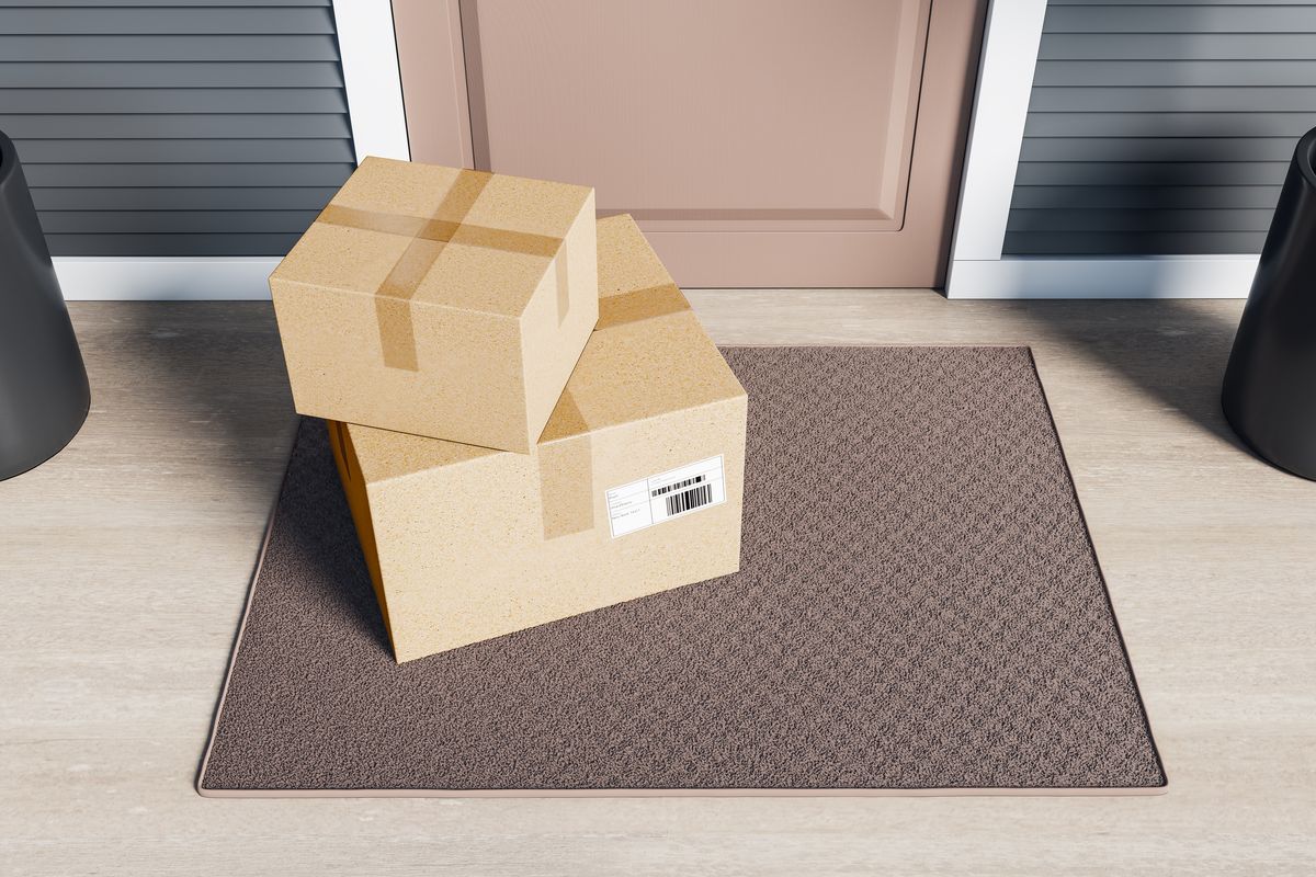 Two cardboard parcels stacked on a brown doormat in front of a house entrance door