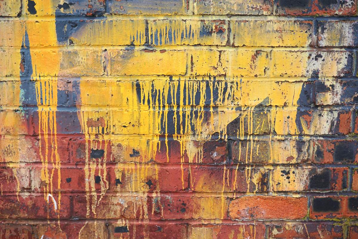 Red and yellow spray paint streaks and drips on a brick wall
