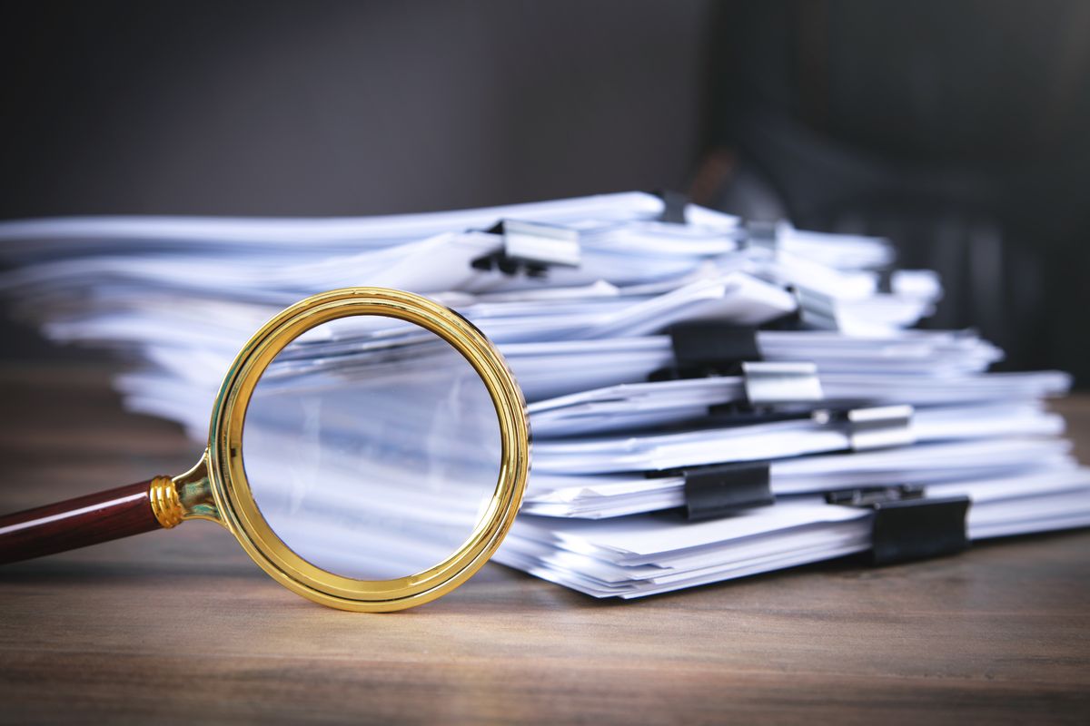 A brass magnifying glass in front of a tall stack of clipped papers.