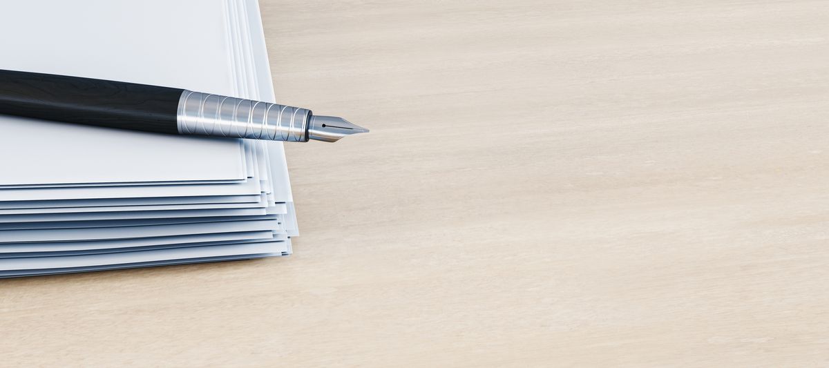 A fountain pen resting on a stack of papers on a wooden desk