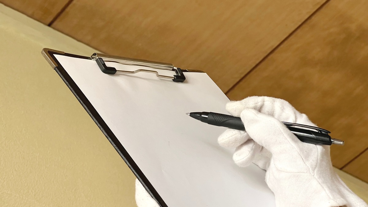 Gloved hand writing on a clipboard