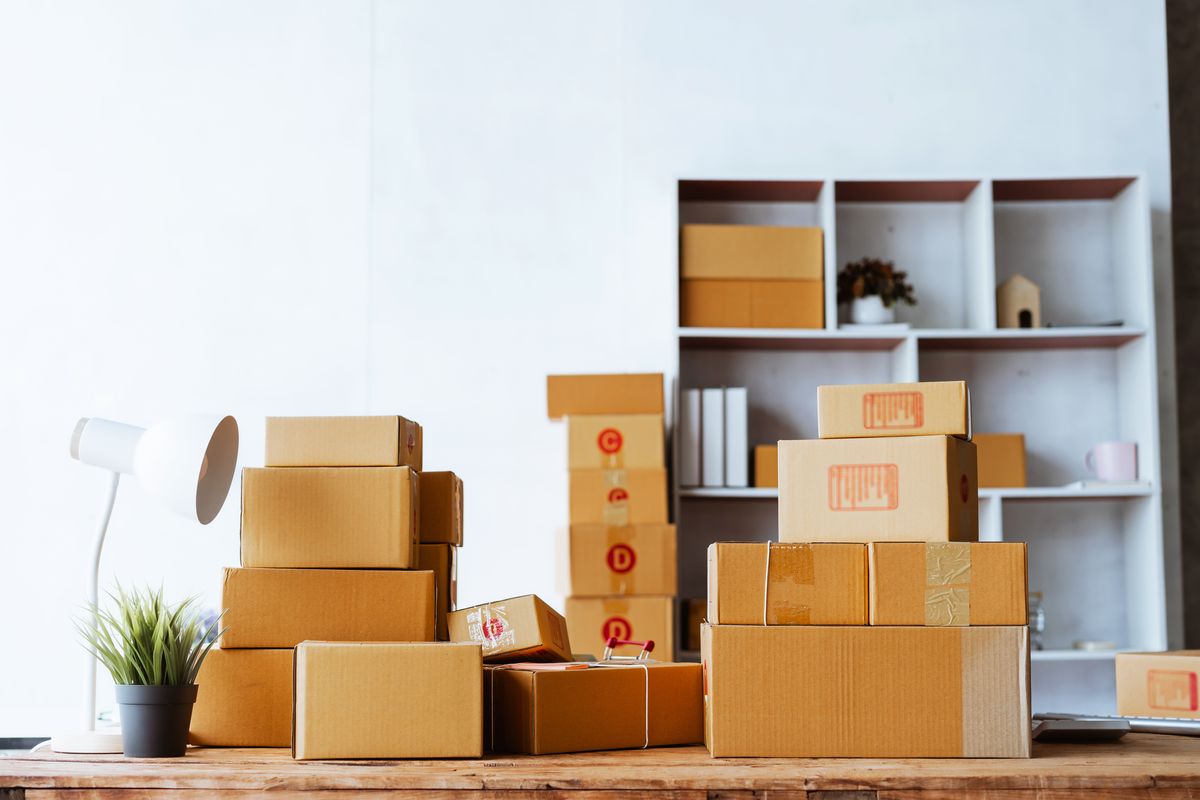 Stacked cardboard storage boxes on a wooden desk beside a white shelf