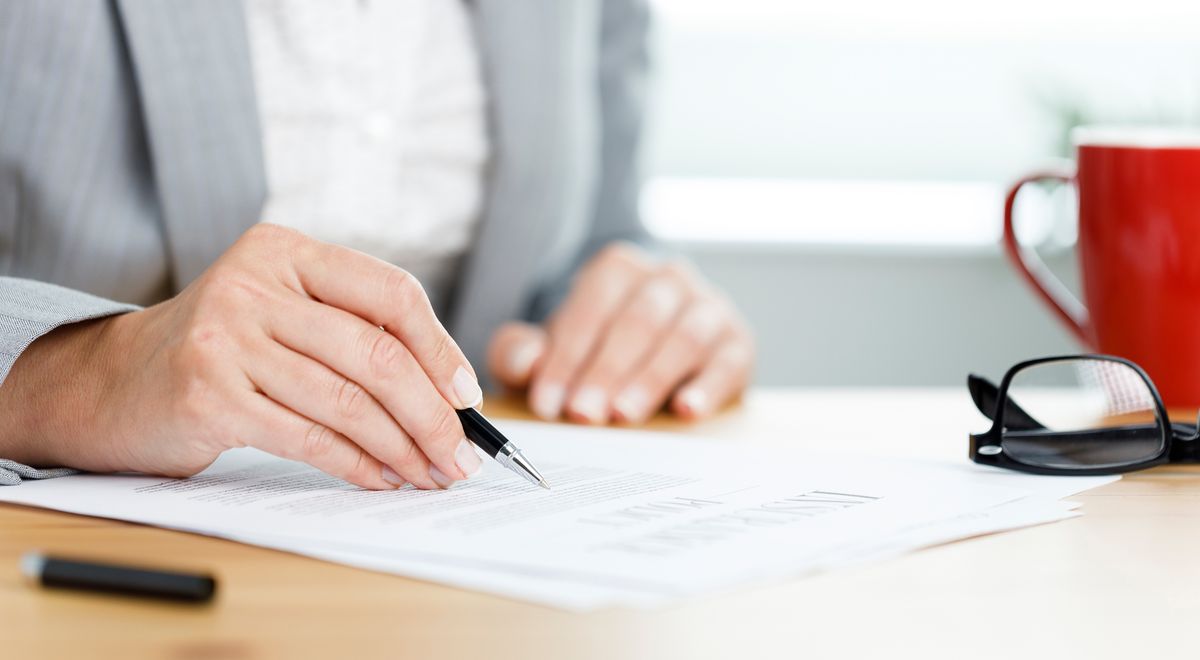 A hand with a pen filling out a form on a desk