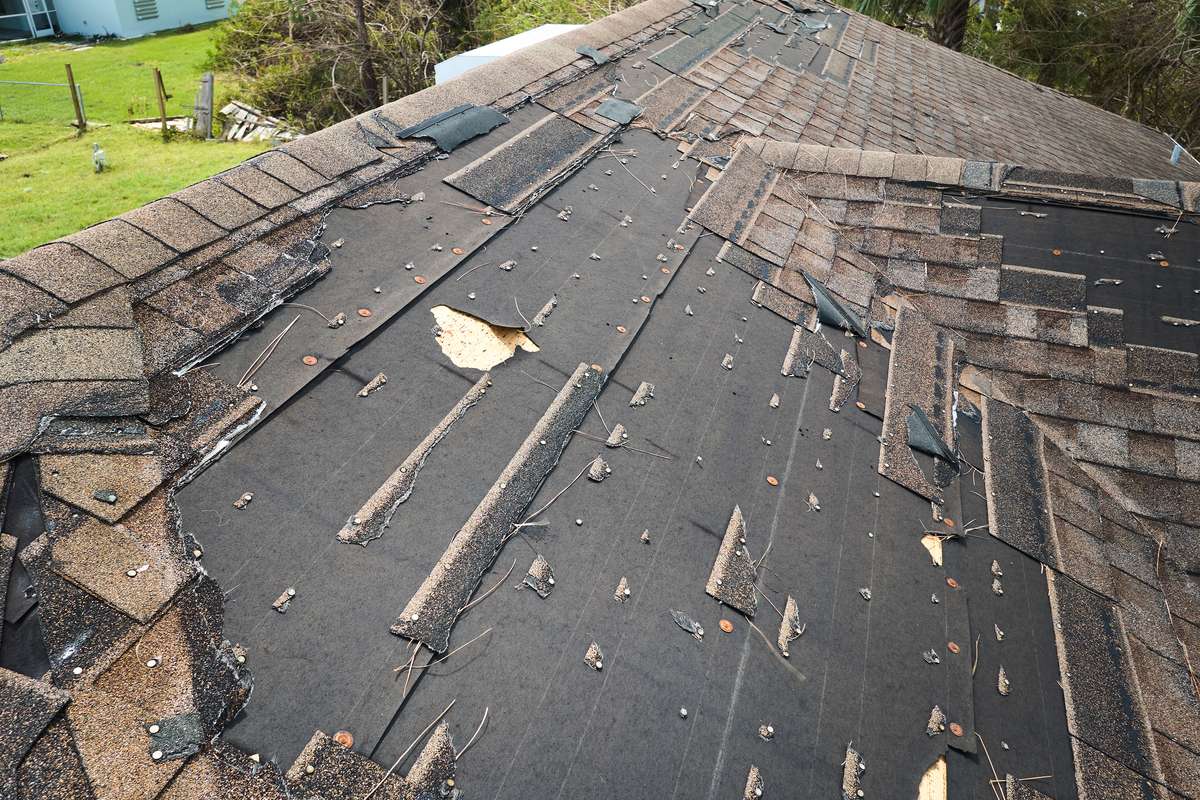 A residential roof with missing asphalt shingles and exposed underlayment after a storm