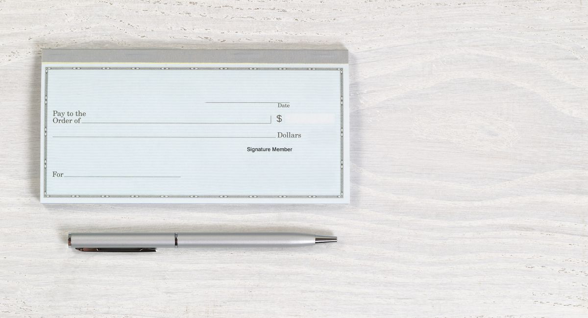 A blank check and a silver pen on a white wooden table